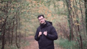 Engaging bearded European man with sharp glasses, standing in a mixed autumn forest, enthusiastically pointing and beckoning viewers closer, inviting them to join a nature exploration journey