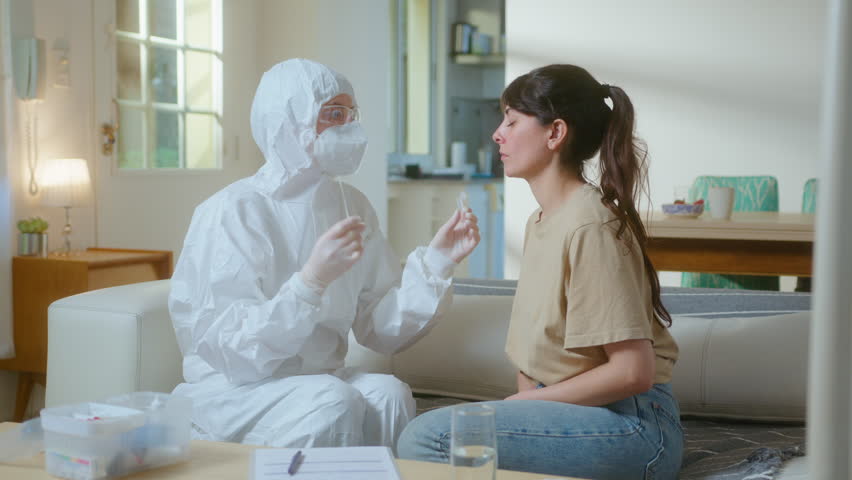 Doctor in protective coverall, mask, eyewear and gloves collecting nasal swab from infected woman, testing patient at home during coronavirus outbreak - Powered by Shutterstock - Get 15% off with code: PIKWIZARD15