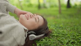 Beautiful young Asian woman relaxed lying on grass wearing headphones listening to music with eyes closed. Relaxed woman lying on the grass listening to music with headphones in a park - Powered by Shutterstock - Get 15% off with code: PIKWIZARD15