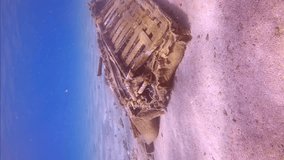 Vertical video, Camera moving forwards approaching to discarded old sofa lying on sandy bottom on shallow water in sunlight, Mediterranean sea, Slow motion. Concept pollution of Ocean