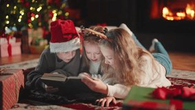 Children siblings reading book in Christmas holidays lying on floor near fireplace, Christmas tree in living ror om at home. Interested sisters brother look in book. Family atmosphere New year Xmas. - Powered by Shutterstock - Get 15% off with code: PIKWIZARD15
