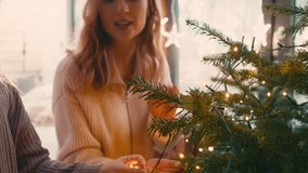 Caucasian woman and her daughter decorating Christmas tree with lights