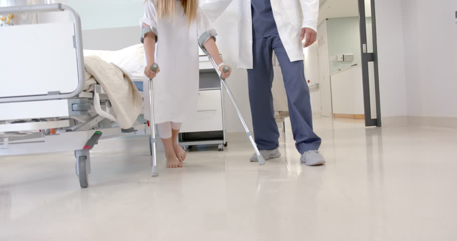 Low section of diverse male doctor helping girl patient use crutches in hospital ward, slow motion. Injury, mobility, childhood, medical services, healthcare and hospital, unaltered. Royalty-Free Stock Footage #1110763197