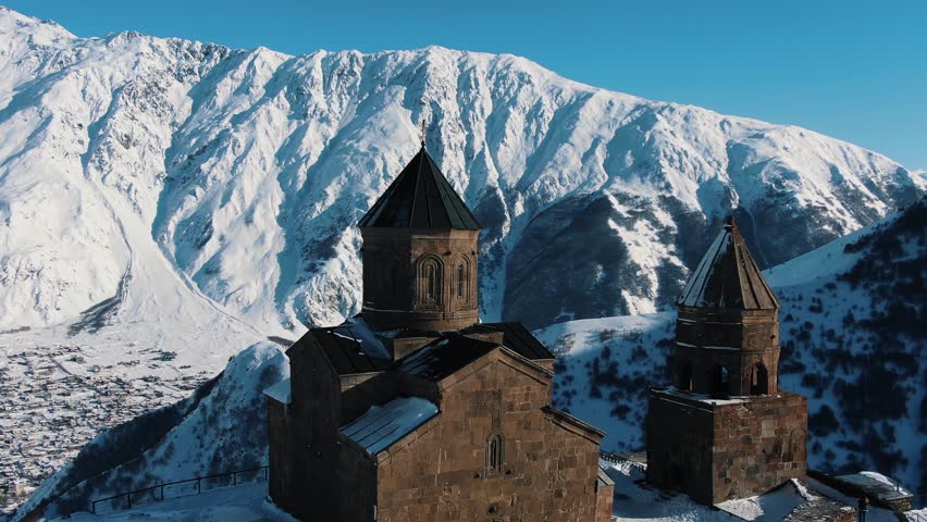 Panorama of the ancient Christian church in Kazbegi in Georgia against the backdrop of snowy high mountains, aerial view. The church in Stepantsminda from a bird's-eye view in winter against the Royalty-Free Stock Footage #1110763829
