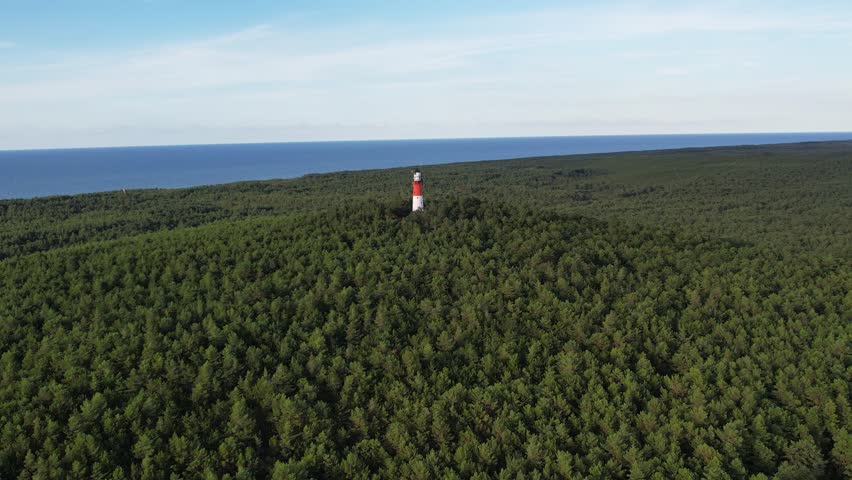 Lighthouse tower at sunny summer day, cinematic aerial view. Drone view of beautiful red white black lighthouse at sea shore, on the top of forested hill, Baltic sea. | Shutterstock HD Video #1110765895