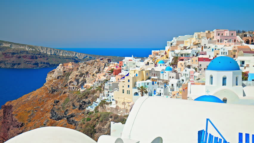 Blue-domed church and white-washed houses in the village of Oia Santorini, Cyclades islands. Panoramic view of traditional and famous houses and churches with blue roofs over the Caldera, Aegean Sea.