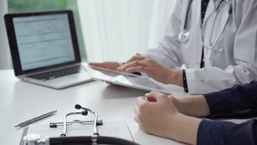 Doctor and patient sitting at the table and discussing something. The pediatrician in a blue dotted blouse and white medical coat using a tablet PC. Medicine concept