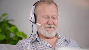 remote communication, an elderly man with a headset talks via video conference on a laptop while relaxing in a cozy room