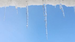 spring drops, a snowdrift with melting icicles hanging from the roof against the blue sky looped video