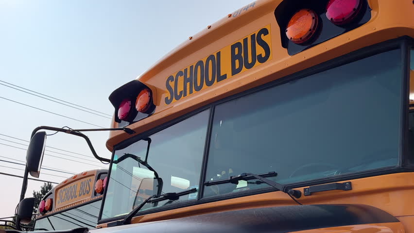 Close-up of a yellow school bus in a parking lot during the day before the end of the school day, waiting for students to take the children home at the end of the day. | Shutterstock HD Video #1110775011
