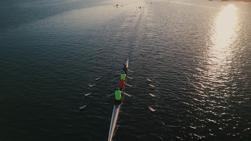 Cinematic shot of a drone on a sports canoe driven by four athletes in an ocean bay, tracking shot. Halifax, Canada. Aerial view of a crew of athletes rowing a boat at sunrise. Royalty-Free Stock Footage #1110775043