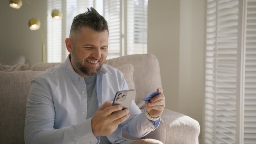Happy guy buying online and throwing card up in air. Male customer making purchase on smartphone. Smiling mature handsome man indoors holding credit card paying online order using mobile banking app Royalty-Free Stock Footage #1110775361