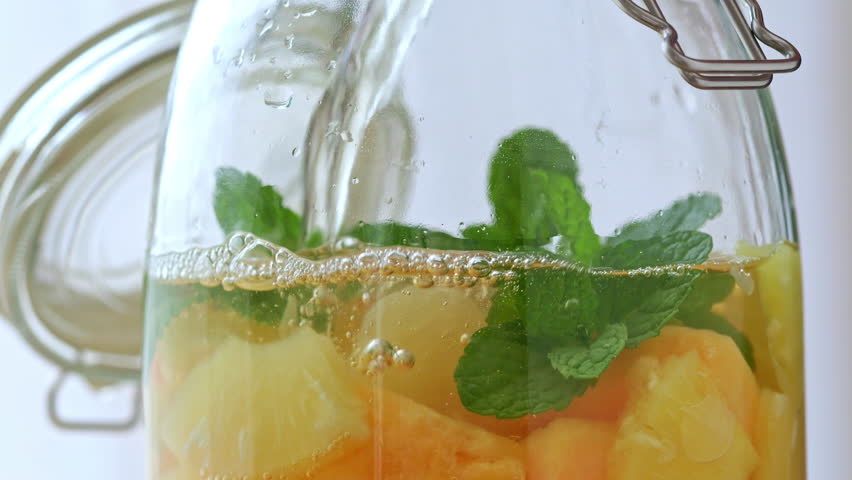 Make white sangria by pouring wine into a glass jar filled with fresh fruit. Fresh mint, pineapple, red-fleshed melon, and grapefruit | Shutterstock HD Video #1110782045