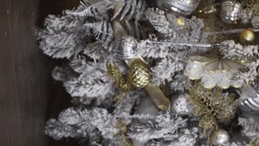 Vertical video of woman is preparing for the xmas holiday and placing gift boxes wrapped in festive gold paper under a luxury decorated Christmas tree. Creative pyramid of winter present for new year.