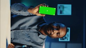 Vertical video Media star holding chroma key product, being sponsored by tech company to film unboxing review. Smiling african american influencer showing mockup screen phone recommendation to