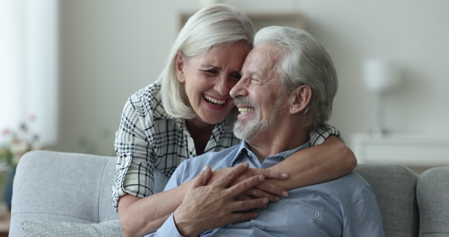 Happy positive senior married couple in love hugging on couch, posing for home portrait, looking at camera, laughing, smiling with healthy white teeth, enjoying romantic relationship, retirement Royalty-Free Stock Footage #1110791339