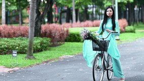 A young girl wearing a cerulean blue ao dai and cycling, the traditional costume of Vietnam. Advertising video for tourism, culture, tradition, beauty of Asian
