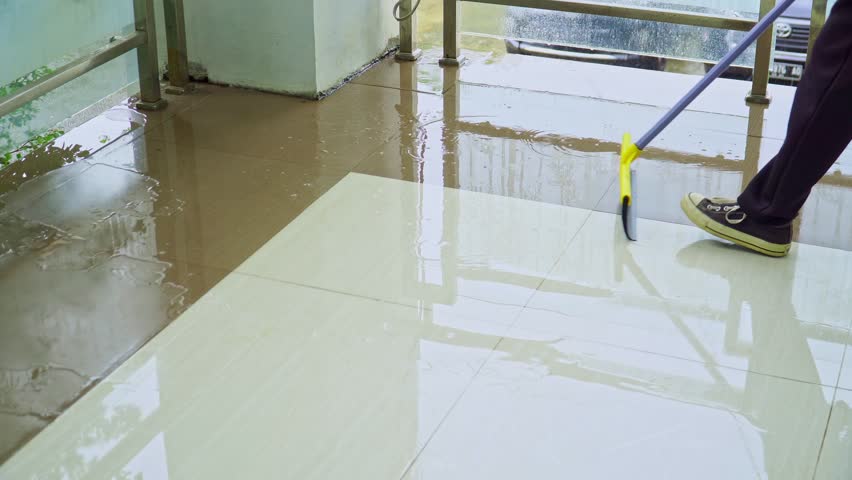 A woman using wiper or squeegee to clean floor surface which was flooded by rainwater. floor scrubbers, cleans using rubber squeegees.  concept of cleaning service. | Shutterstock HD Video #1110796353