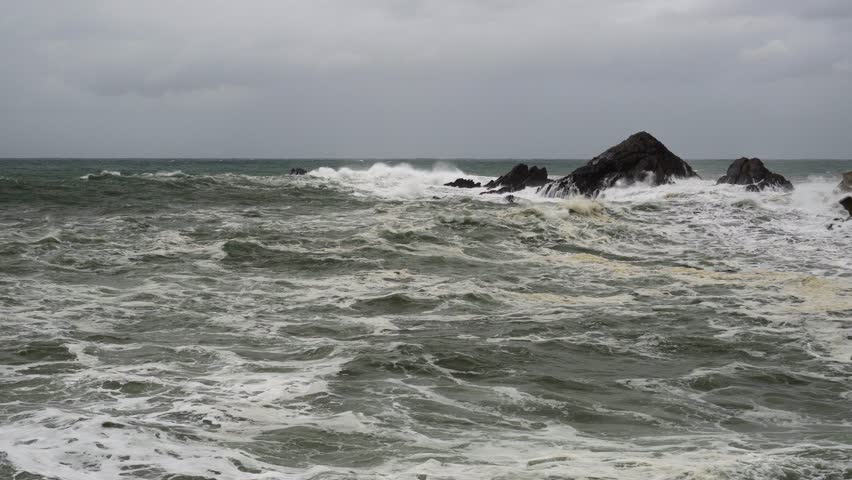 static shot of rough and dangerous sea with large waves breaking against the harbor and rocks due to a storm and strong winds. 