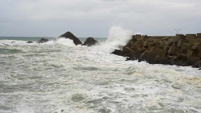 Static shot of rough and dangerous sea in slow motionwith large waves breaking against the harbor and rocks due to a storm and strong winds. 