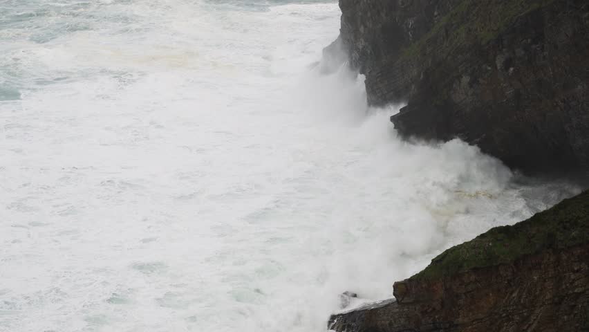 Zenithal view of a sea with large windstorm waves impacting against the cliff and rocks. Concept of erosion and danger of the sea.