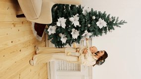 mother smiles and holds a baby in her arms who reaches for toys in the form of white flowers on a Christmas tree at home. vertical video