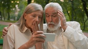 Close up portrait shocked worried aged pensioners man woman old Caucasian couple sitting bench looking phone screen outside in park reading bad news smartphone error family unpleasant message internet - Powered by Shutterstock - Get 15% off with code: PIKWIZARD15