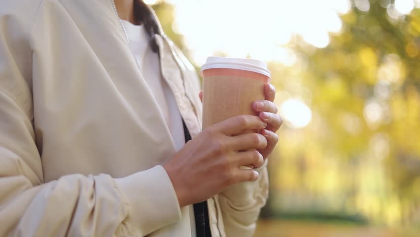 Unrecognisable young woman holds take away eco paper cup with recycle lid hot drink, coffee or tea, warms hands in autumn park, cold day. Beverage to go. Happy zero waste lifestyle concept. Royalty-Free Stock Footage #1110811931