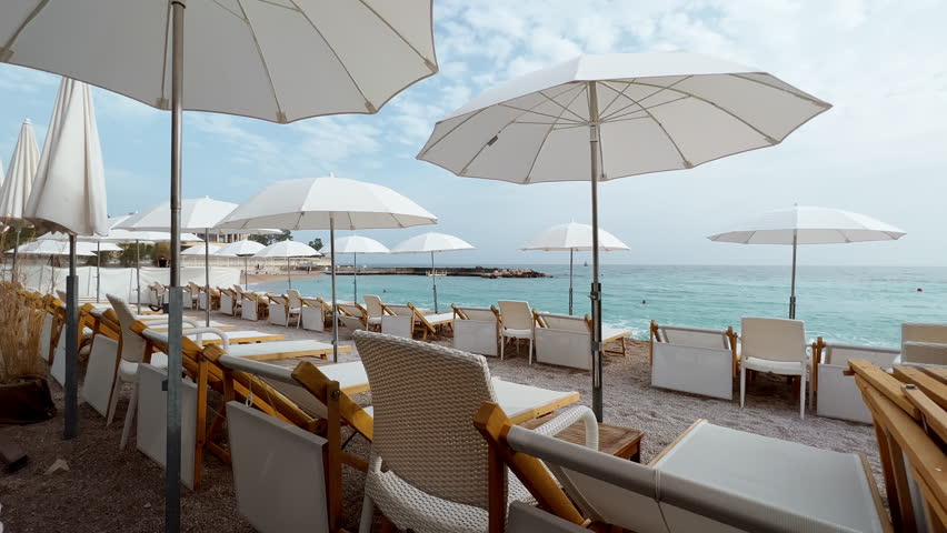The famous beach Larvotto of principality of Monaco in sunny day, sun umbrellas, palm trees, azure water