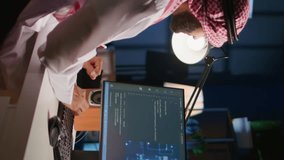 Vertical video Experienced developer updating neural networks, writing intricate binary code scripts on computer. Muslim worker uses digital device programming to upgrade AI simulation model