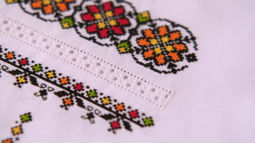 Texture of linen white fabric with an embroidered element. Cross stitches with colored threads and artfully made hemstitching. Ukrainian embroidery pattern for folk shirt.