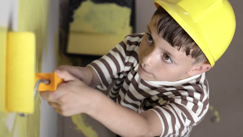 Cute boy with a paint roller. Happy kid helps parents to paint wall. Home renovation.