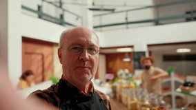 Local neighborhood supermarket elderly owner films promotional vlog showing high quality organic vegan products. Entrepreneur doing marketing video presenting fresh produce in his zero waste store