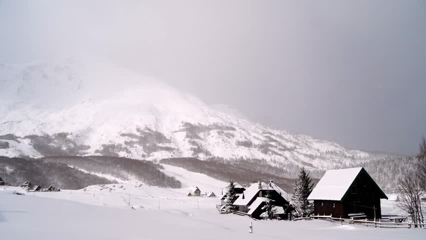 Wooden houses at the foot of the mountains under snowfall