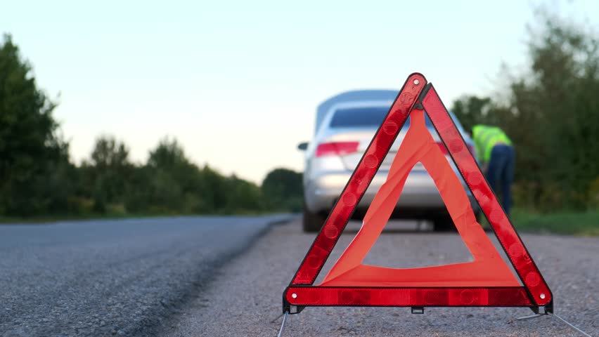 Unrecognizable sad driver in reflective vest. Male driver standing near broken car with open up hood. Red triangle to warn other road users of car breakdown or engine failure stop at countryside Royalty-Free Stock Footage #1110850513
