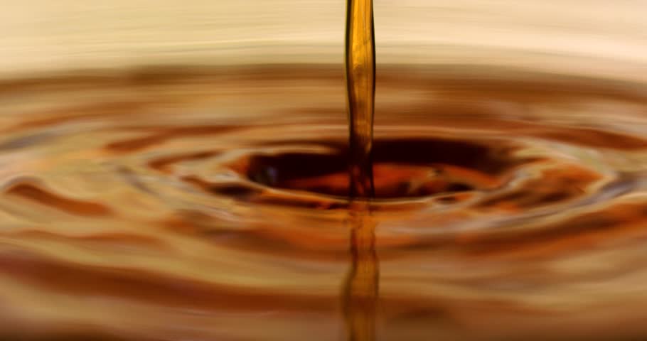 Macro shot of a light brown coffee stream being poured into a cup.