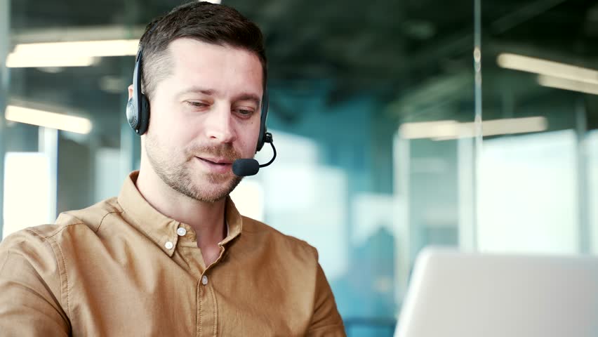Close up. A corporate operator who works in customer support speaks on a video call using a laptop. Call center agent in wireless headset helping clients with complaints in office. Online consultation Royalty-Free Stock Footage #1110852831