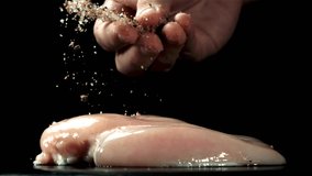 A man sprinkles spices on chicken fillet. Filmed on a high-speed camera at 1000 fps. High quality FullHD footage