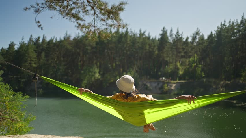 relaxed woman swinging in hammock on mountain lake shore in forest. wanderlust, summer vacation, travel outdoors, active leisure. happy girl is resting in a summer forest on a green hammock Royalty-Free Stock Footage #1110865235