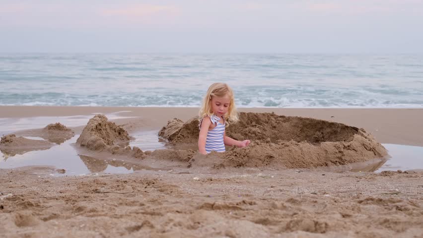 Little girl with long hair playing with sand on beach building castle at Mediterranean seaside in Spain. Carefree childhood, happiness concept. Royalty-Free Stock Footage #1110865707