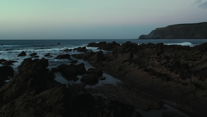 Young man walking along the coastline and taking pictures of the cliffs in Portugal during sunset.