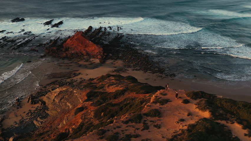 Young man walking along the coastline and taking pictures of the cliffs in Portugal during sunset.