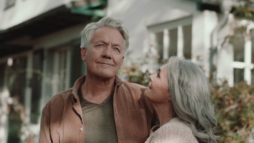 Senior couple stands content in front of their house during autumn