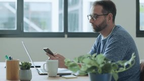 Businessman sitting at desk with laptop looking at smartphone - Powered by Shutterstock - Get 15% off with code: PIKWIZARD15