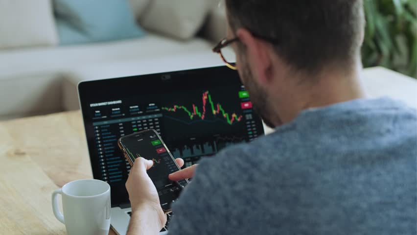 Businessman looking at smartphone and laptop with stock market charts - Powered by Shutterstock - Get 15% off with code: PIKWIZARD15