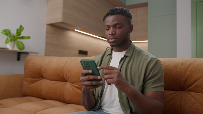 Black Man Reading Bad News on his Cellphone at Home. Desperate young adult male using phone on couch. Royalty-Free Stock Footage #1110872295