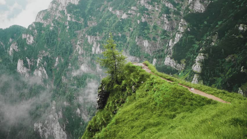 Slow motion static zoom-in shoot of a panoramic viewpoint on Caraiman Mountain, a steep hiking pathway crossing deep valleys and vertical rock walls in the Bucegi Carpathian Mountains.