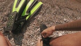 POV shot, guy puts on diving boots, takes fins in his hand and goes into sea. First person video, man takes snorkeling equipment and goes into Mediterranean sea