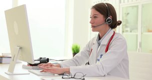 Female general practitioner wearing headphones with a microphone gives remote consultation to patient via video call. Therapist cardiologist participates in professional knowledge at online conference