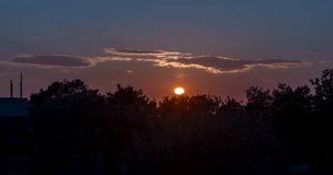 Title: Time-lapse video of a sunset over land with fast-moving clouds and bushes in the foreground

